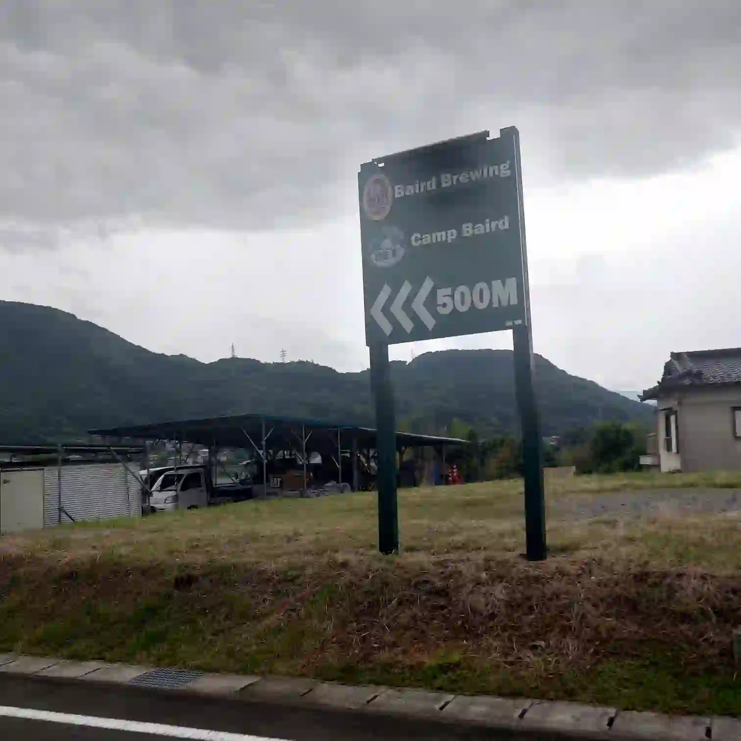 ベアードブルーイングとキャンプベアードまで500mの案内看板（山を背景に）