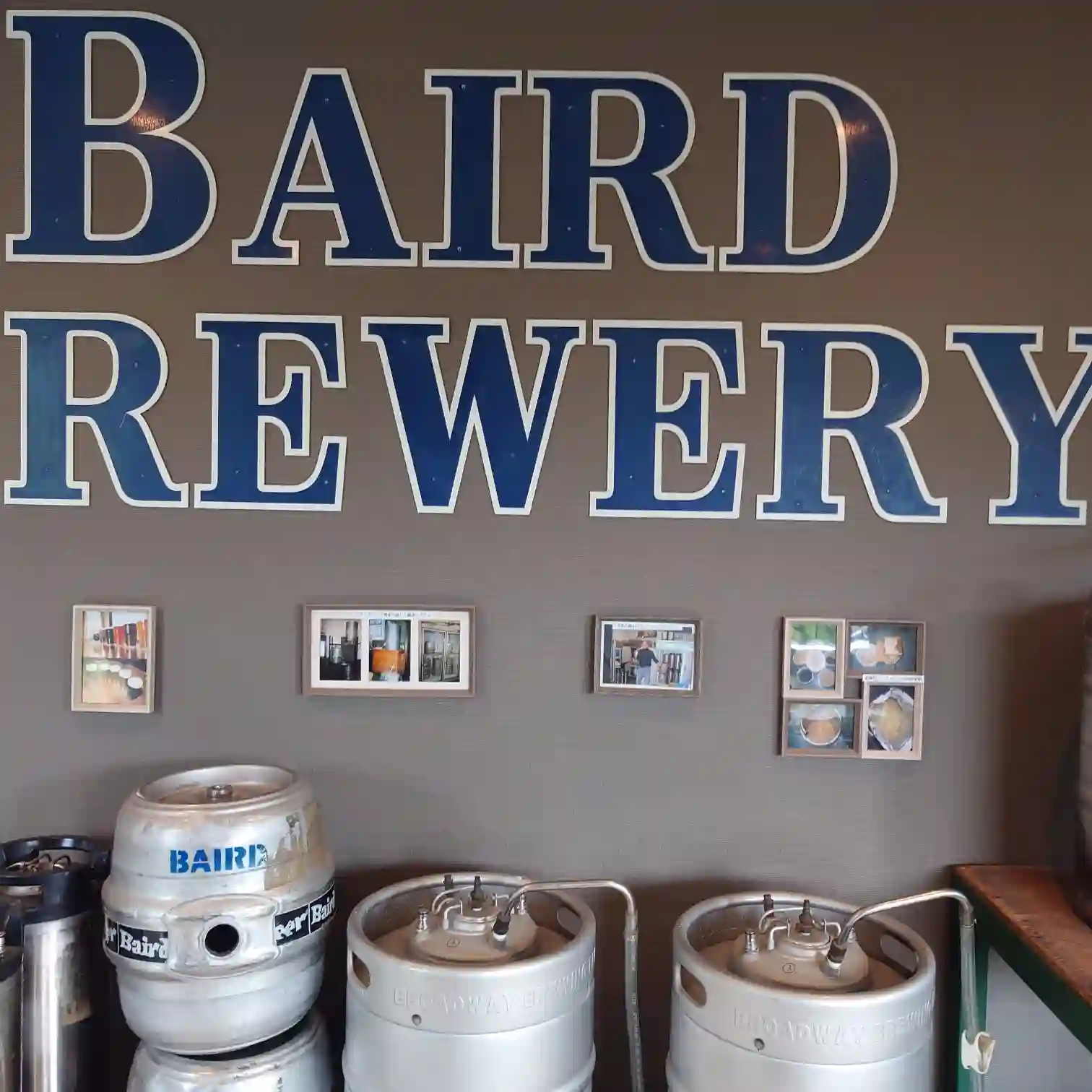 「BAIRD BREWERY」のロゴが大きく描かれた壁面と、展示されたクラフトビールのステンレス樽。伊豆修善寺のブルワリー施設内の様子。