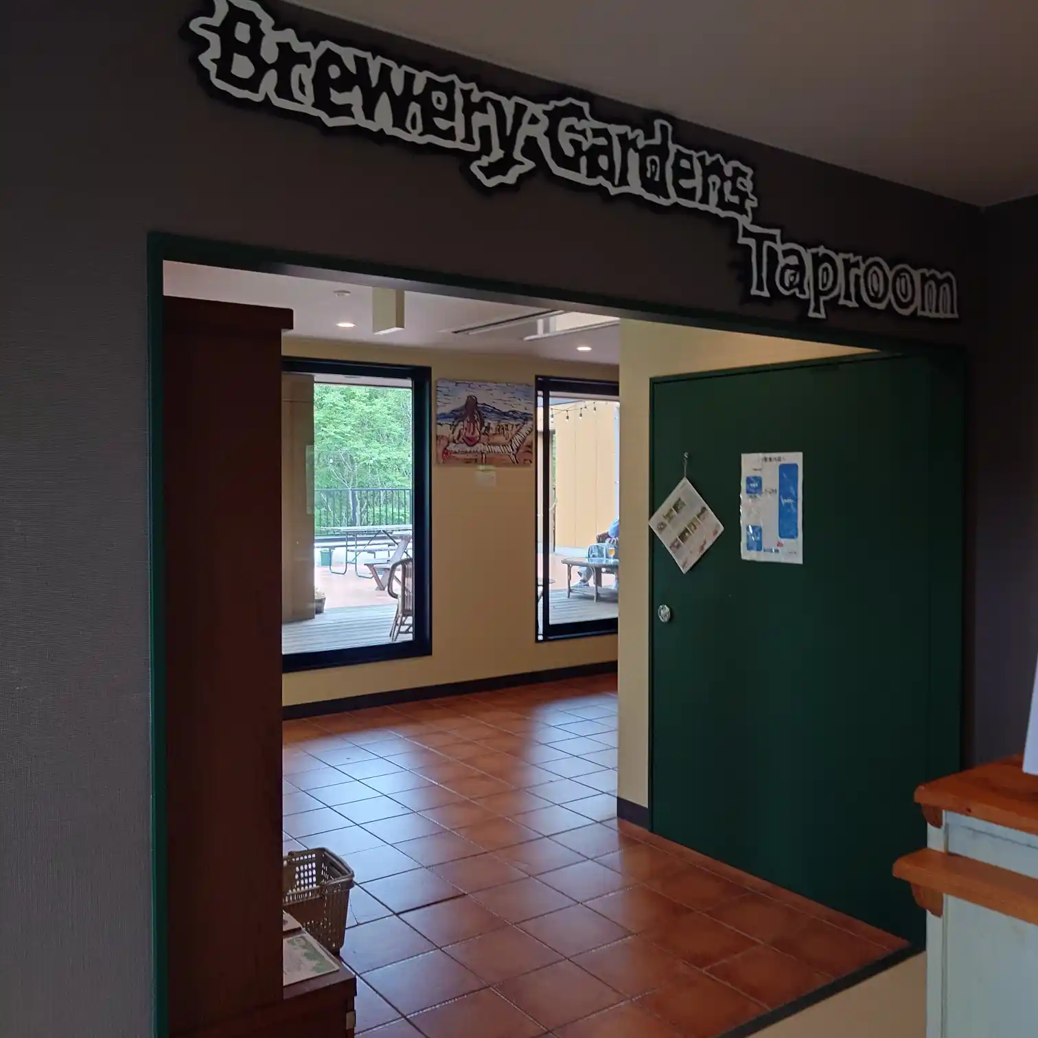 ベアードブルワリー修善寺の「Brewery Gardens Taproom」内観。緑に囲まれたテラス席が窓越しに見え、クラフトビールが楽しめる開放的な空間が広がる。