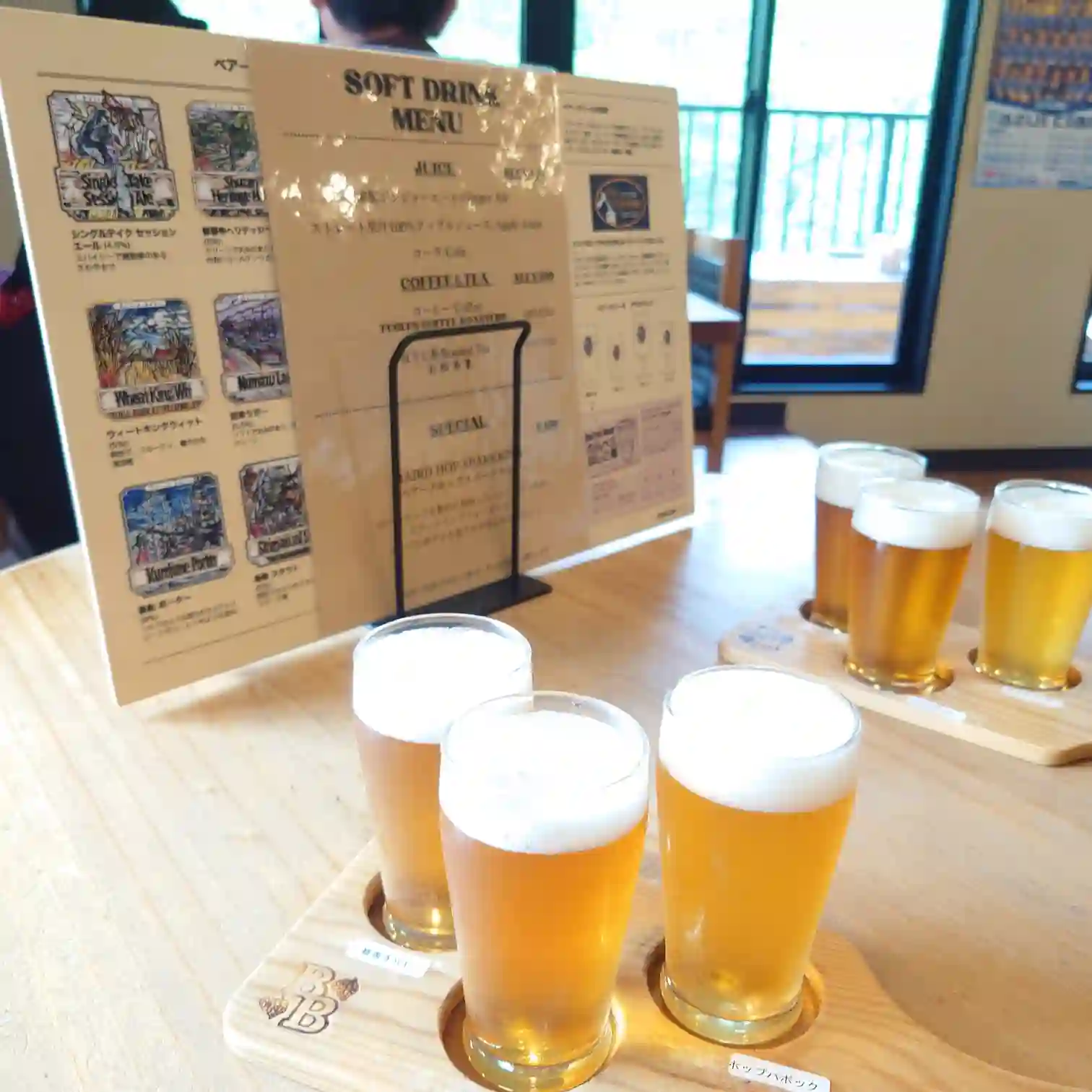 修善寺のベアードブルワリーで提供されるクラフトビールのテイスティングセットとソフトドリンクメニューの様子。木製の専用プレートに注がれた4種のビールで飲み比べが楽しめる。