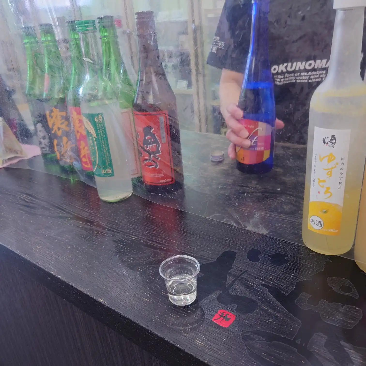 奥の松酒造の試飲カウンターと並ぶ日本酒ボトル、試飲用カップ