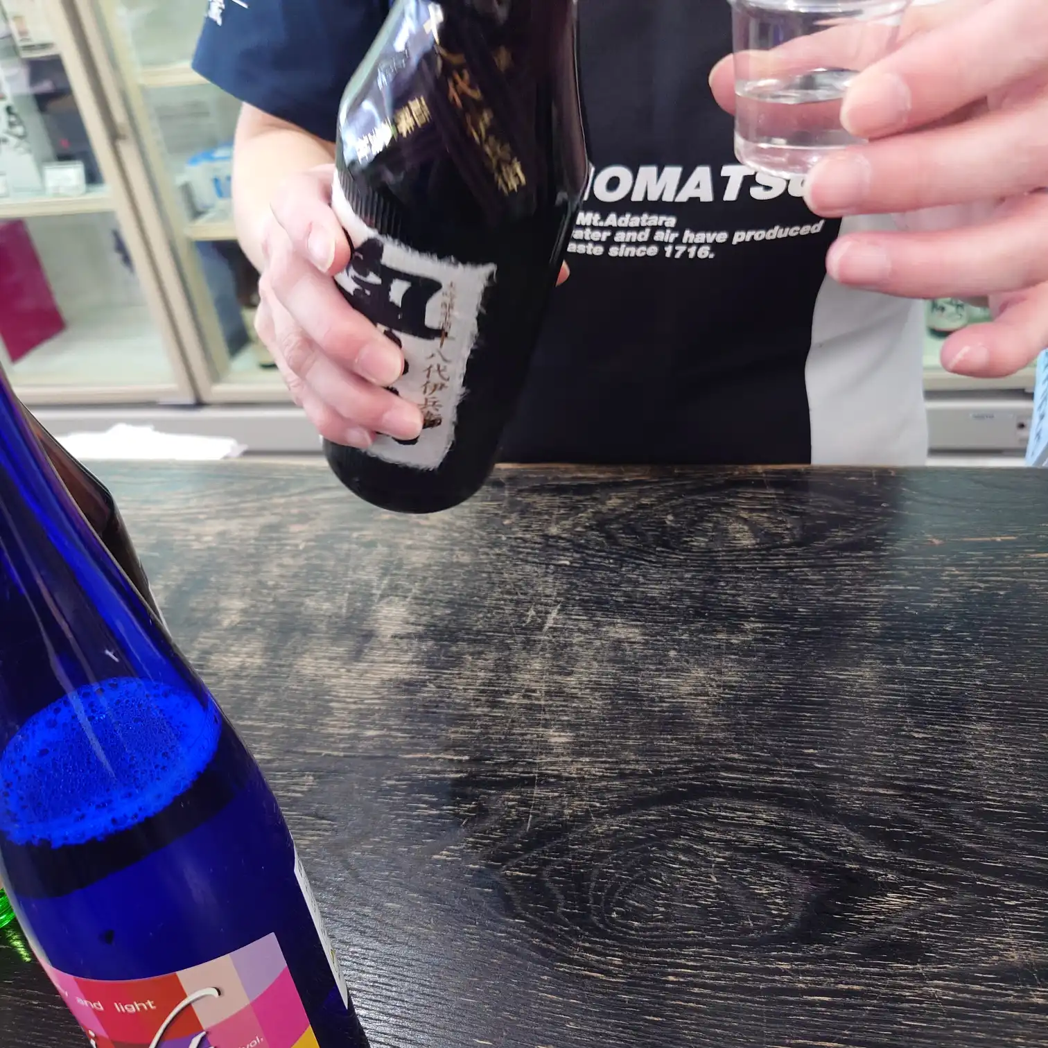 奥の松酒造の試飲カウンターでスタッフが日本酒を注ぐ手元