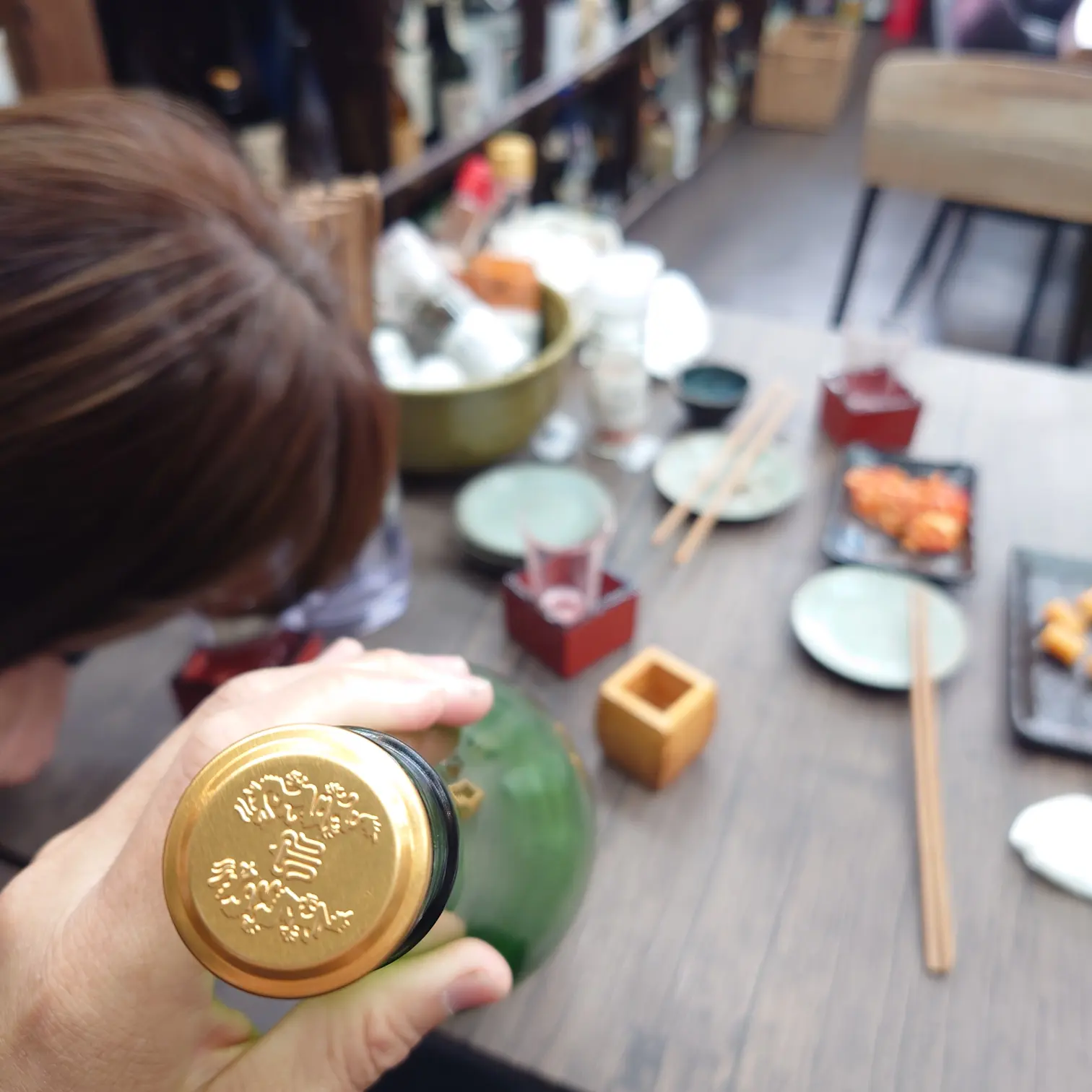 十四代 槽垂れ 本生の金色キャップを手にした瞬間。枡や小皿が並ぶテーブル風景|熱海ミニ横丁(伊豆半島合同会社)