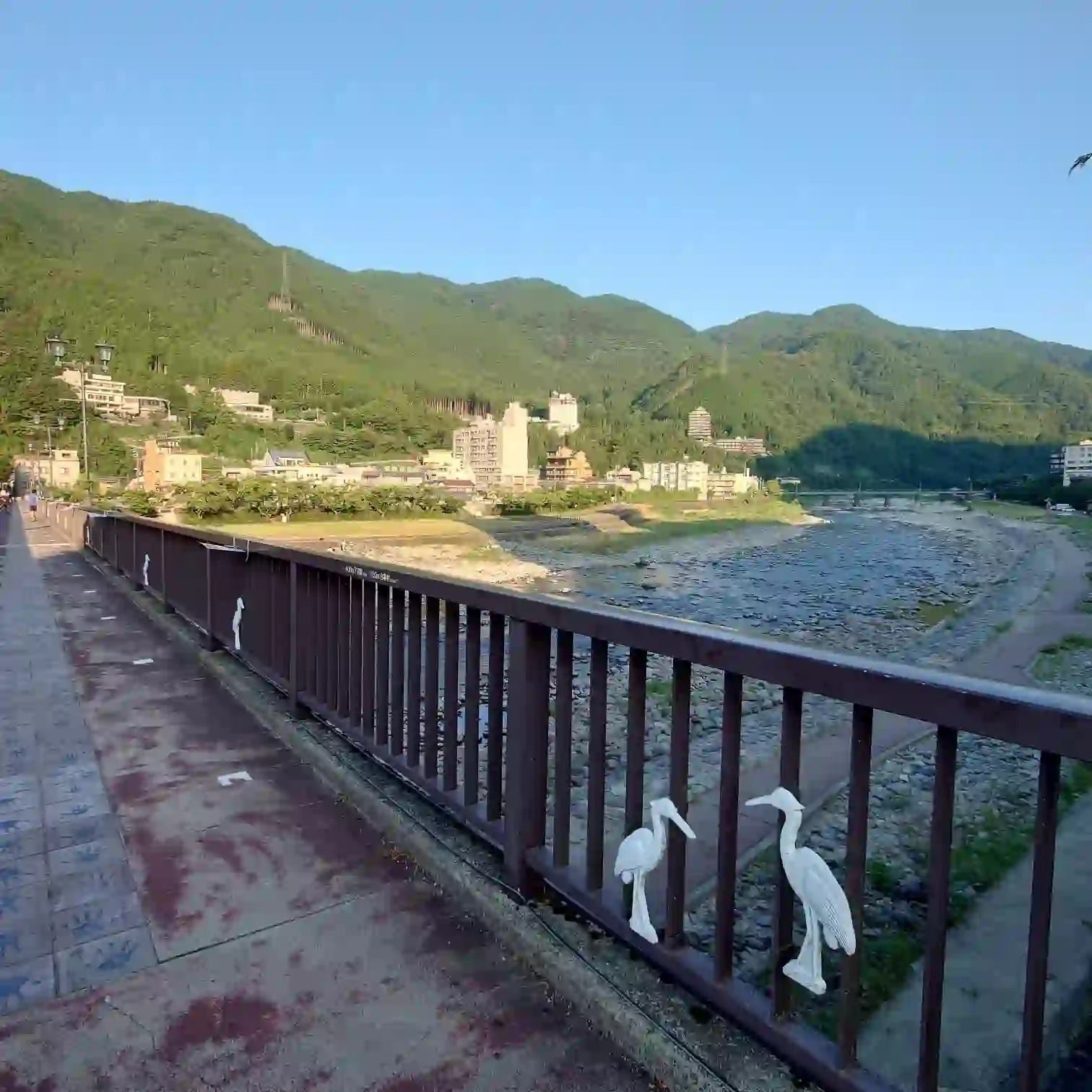 下呂温泉・飛騨川に架かる橋の欄干に白鷺モチーフ、温泉街と緑の山並みを望む早朝のランニングルート──広い歩道で走りやすい川沿い景色