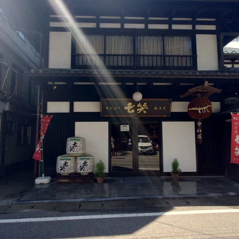 木曽・中山道沿いに佇む七笑酒造の酒蔵外観。杉玉と酒樽が並ぶ伝統的な黒塗りの建物