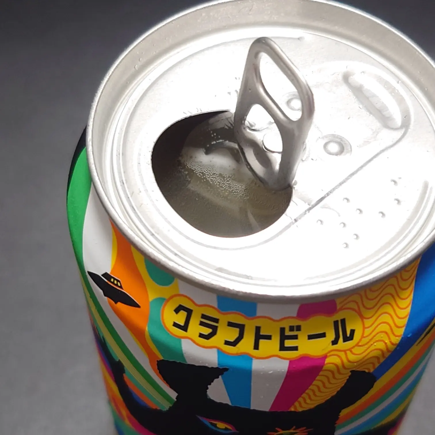 ヤッホーブルーイング『有頂天エイリアンズ HAZY IPA』の開栓後の缶上部アップ。プルタブの開口部から冷えたビールが見え、カラフルなデザインと「クラフトビール」の文字が映る。