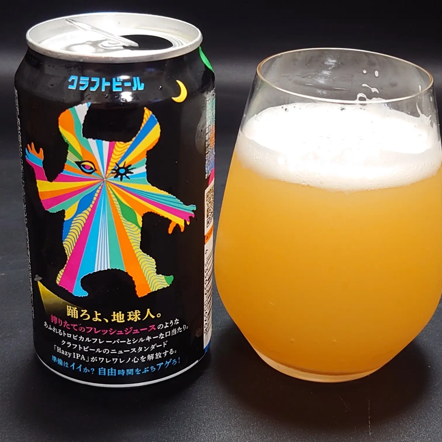 ヤッホーブルーイング『有頂天エイリアンズ HAZY IPA』の缶（裏面のカラフルなエイリアン絵柄と説明文）と、グラスに注いだ濁りあるオレンジ色のビールと白い泡。