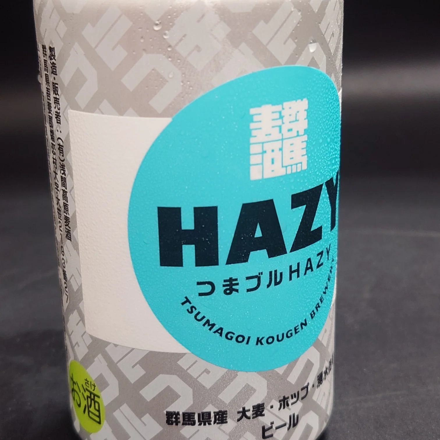 つまブル HAZYの正面ラベル。ターコイズの円に大きく「HAZY」、下に「つまブル HAZY」。左下に緑の「お酒」マーク、水滴のついた缶。