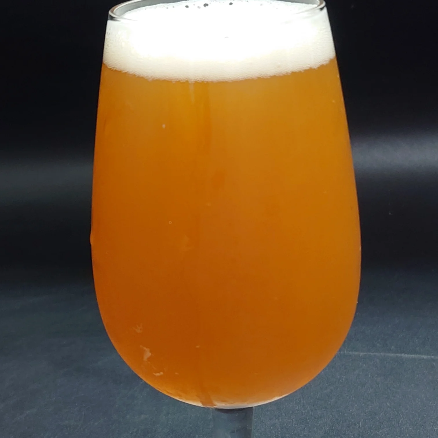 グラスに注いだつまブル HAZY。濁りの強いオレンジ色の液面と白い泡のヘッド。