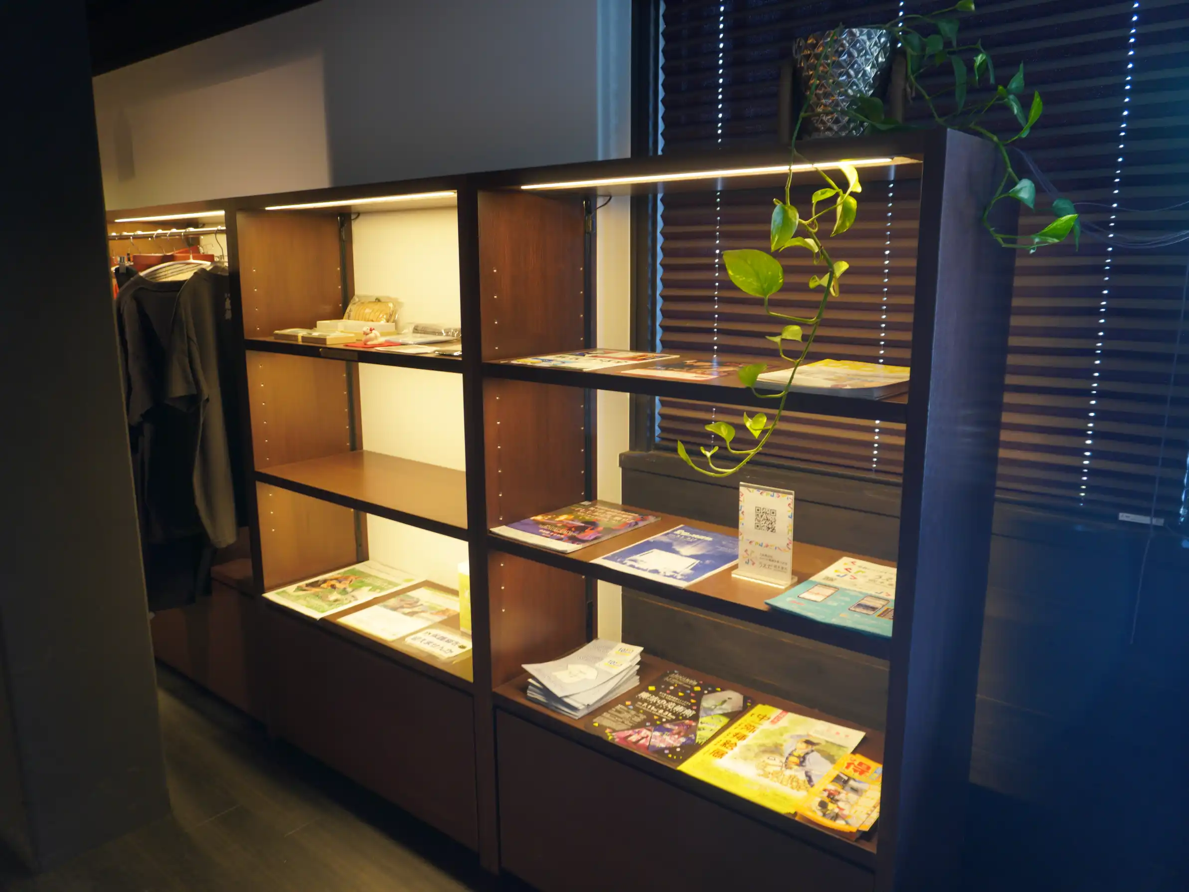 岡崎酒造売店のパンフレット棚。観光リーフレットや案内冊子が並び、上段にはポトスのツタ