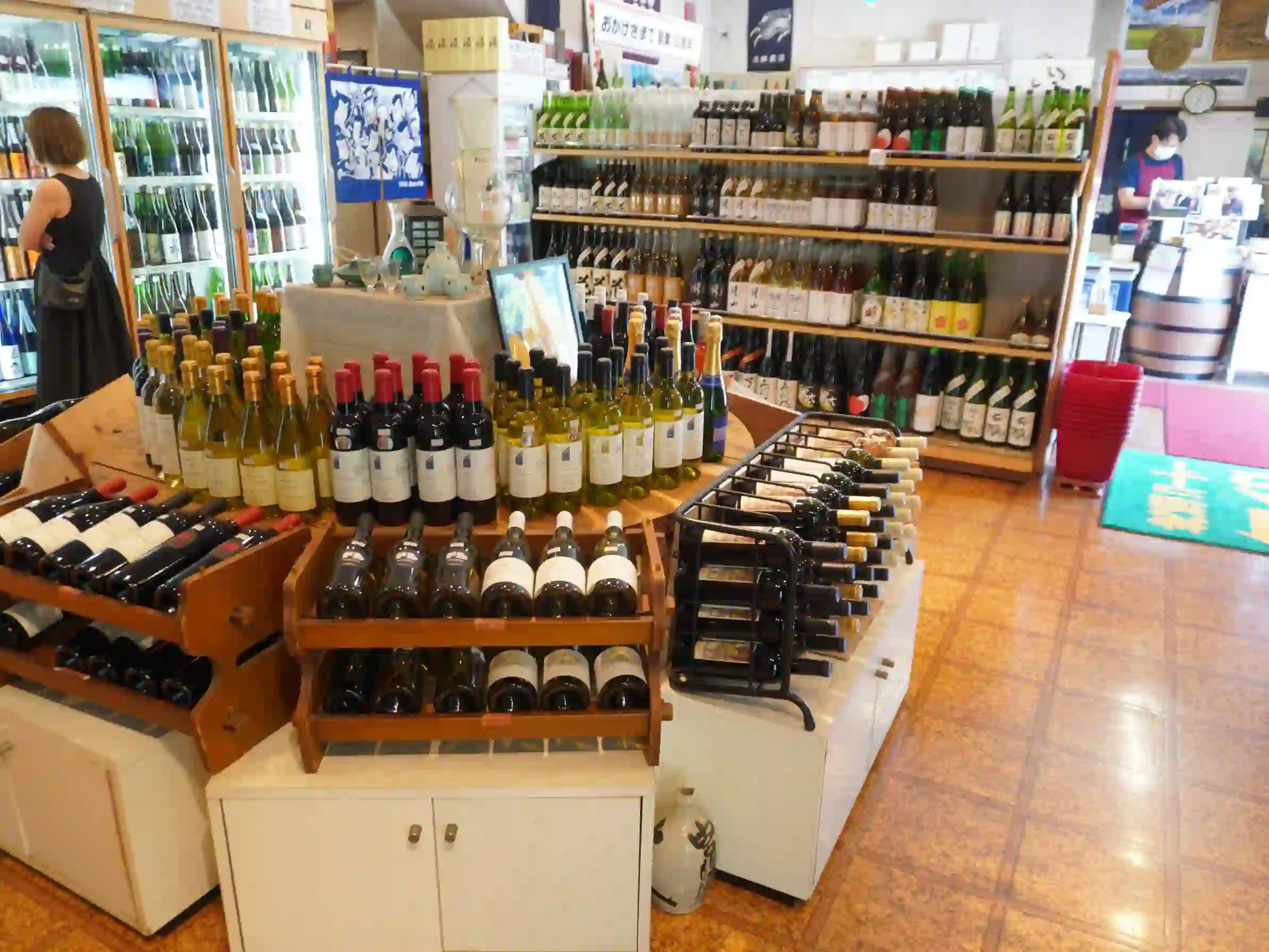 店内中央にワインの平台什器。周囲に日本酒棚と冷蔵庫が並び、レジカウンターが見える。