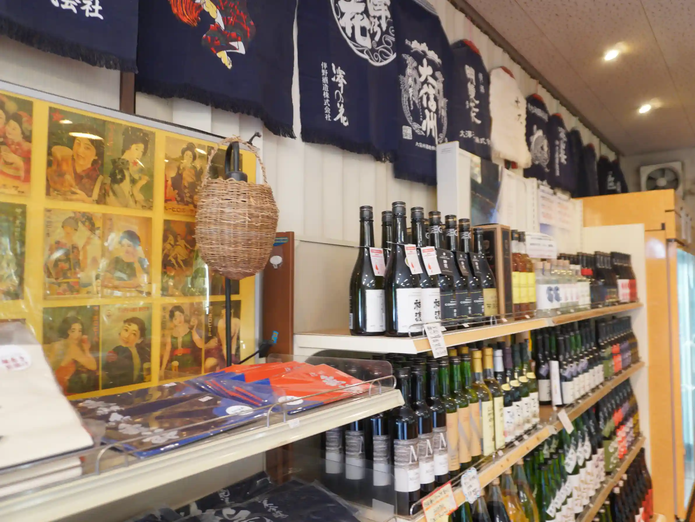 店内の酒棚と前掛け、左にレトロポスターと酒器小物。