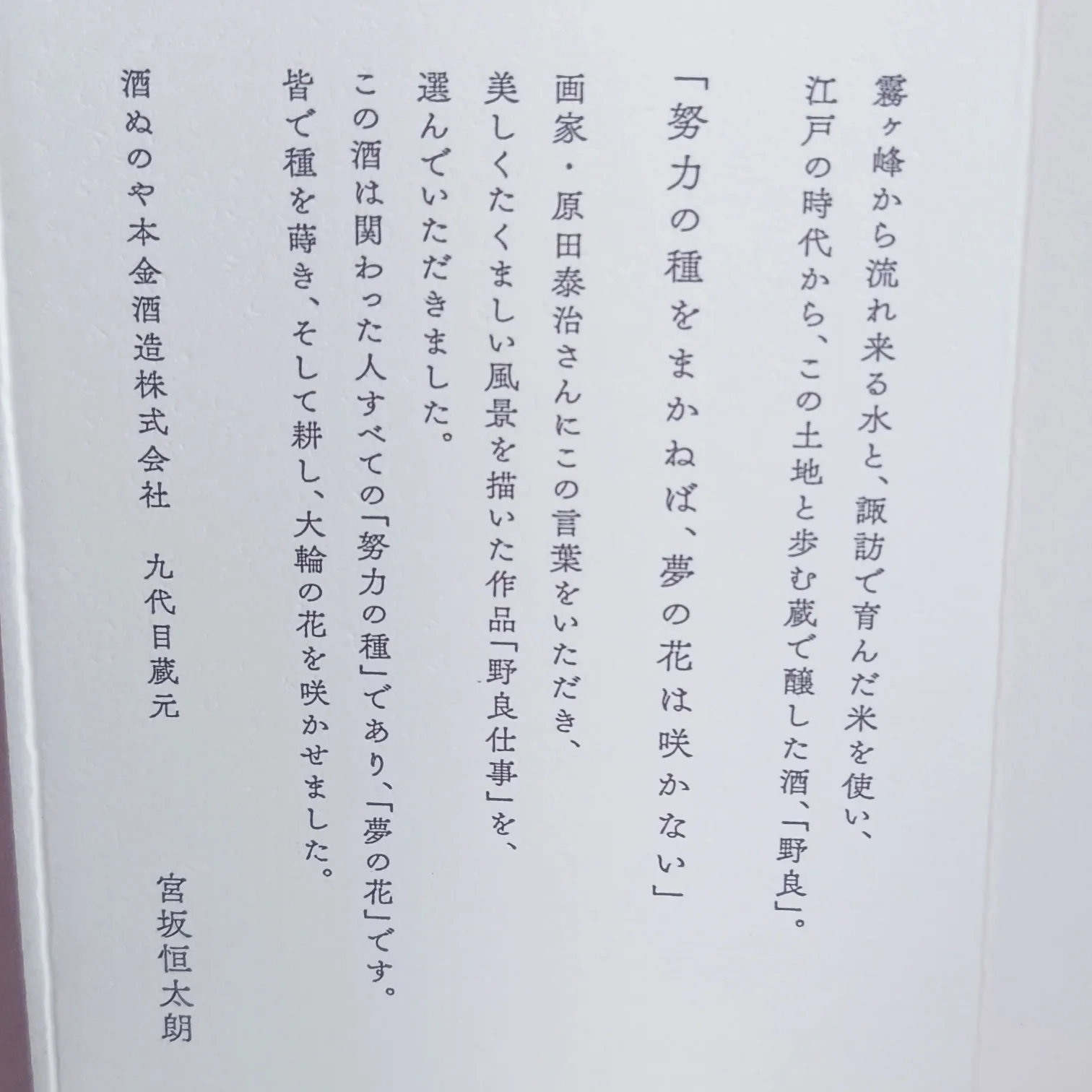 日本酒「野良 Nora」本金の側面ラベル—霧ヶ峰の水と諏訪米で醸す酒、原田泰治の作品「野良仕事」を採用し「努力の種をまかねば夢の花は咲かない」の言葉が添えられた説明文
