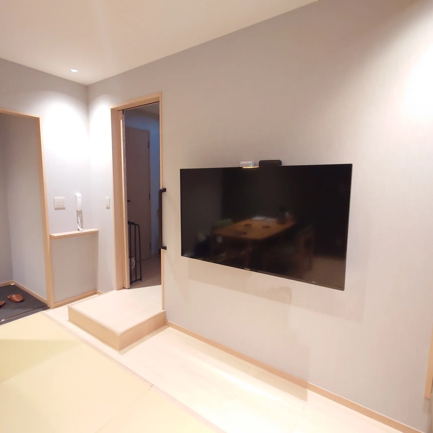 リビング壁面の大型壁掛けテレビ。奥に玄関とダイニングテーブル。