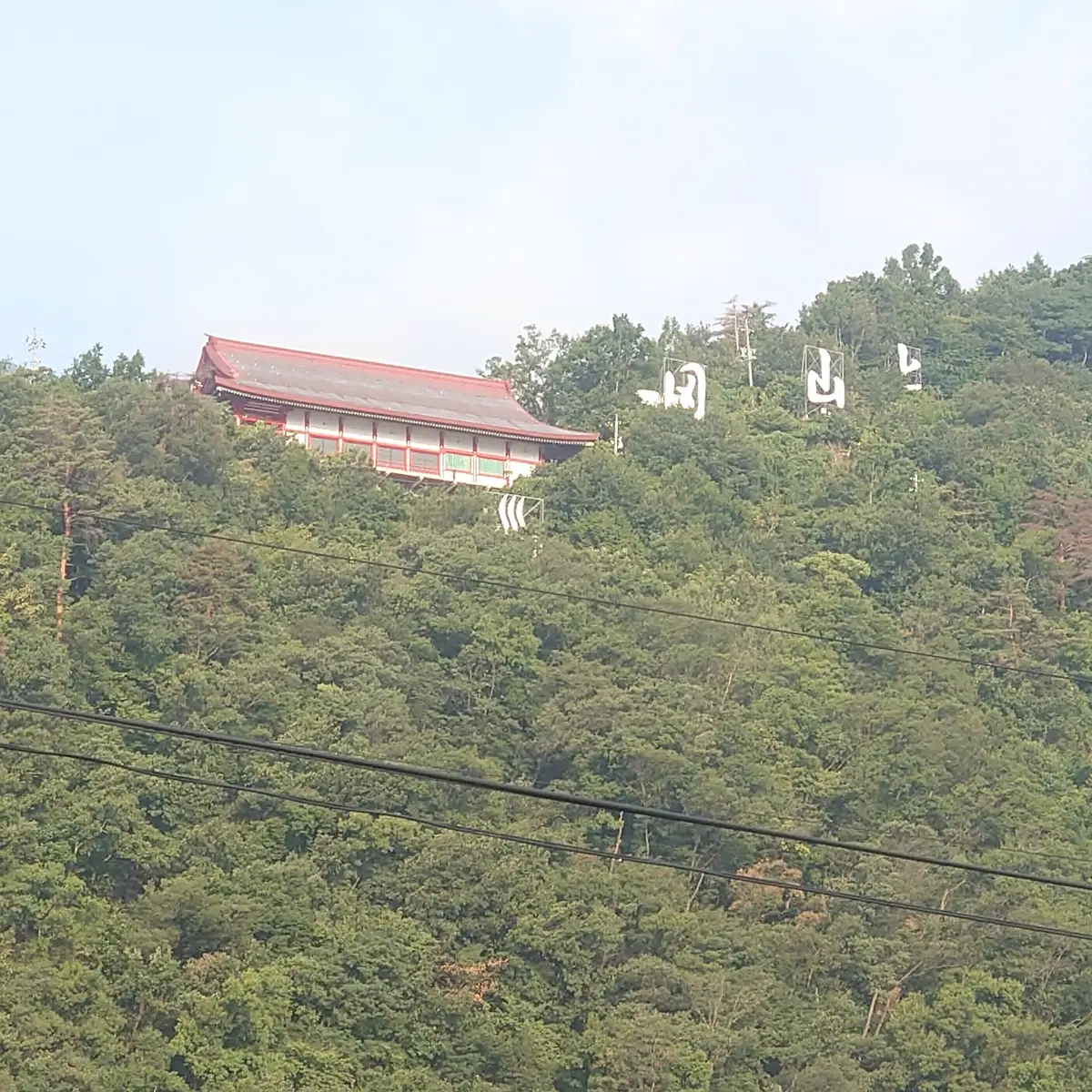 山の緑に包まれた斜面に建つ城山善光寺と大きな白文字の看板