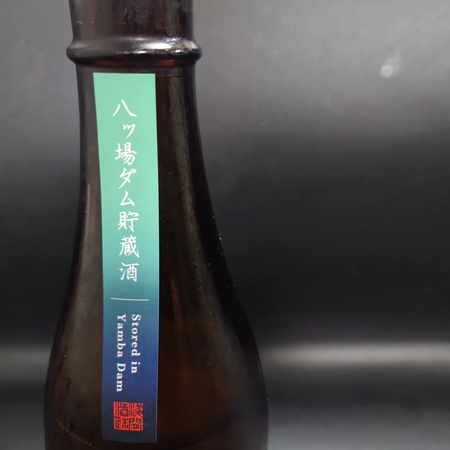 八ッ場ダム貯蔵酒|ボトル首の縦ラベル接写(Stored in Yamba Dam) 群馬・八ッ場ダムで熟成された日本酒「貯蔵酒」のボトル首に貼られたグラデーション縦ラベルを正面から接写した写真