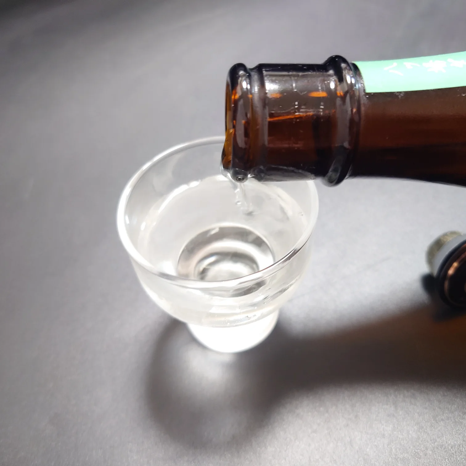 八ッ場ダム貯蔵酒|お猪口に注がれる透明な酒液 八ッ場ダム貯蔵酒をガラスのお猪口に注いでいる瞬間を切り取った写真、透明感のある酒液が静かに流れ込む様子