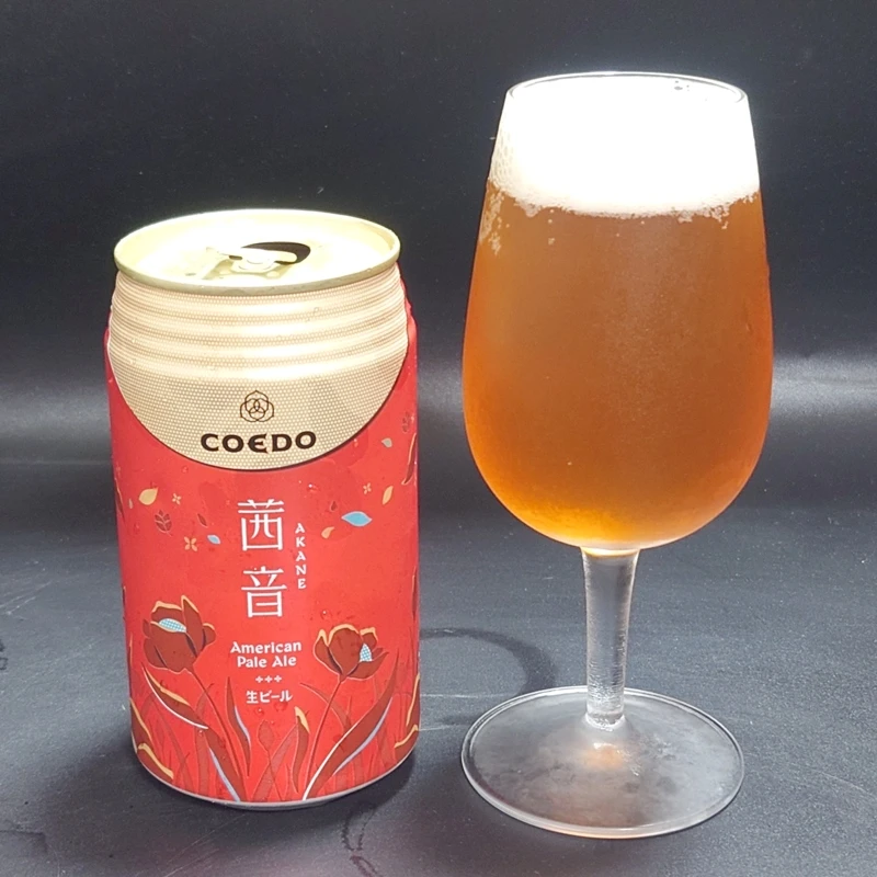コエドビール アカネの缶とグラス(American Pale Ale/琥珀色と白い泡) 埼玉のクラフトビール・コエドビール「アカネ」American Pale Ale、赤い和柄デザインの缶と琥珀色のビールを注いだグラスを黒背景で並べて撮影(白い泡のヘッド)