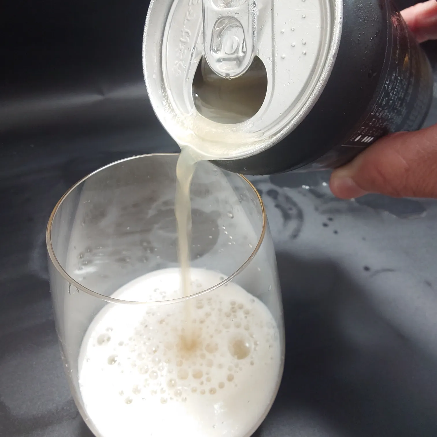 宇宙ビール 注ぎの瞬間 クリーミーな泡とヘイジーな色合いのアクションカット UCHU BREWING 宇宙ビールを缶からグラスへ注ぐ瞬間 ヘイジーな淡い色とクリーミーな泡 しずくの残る缶口と手元の動きがわかる