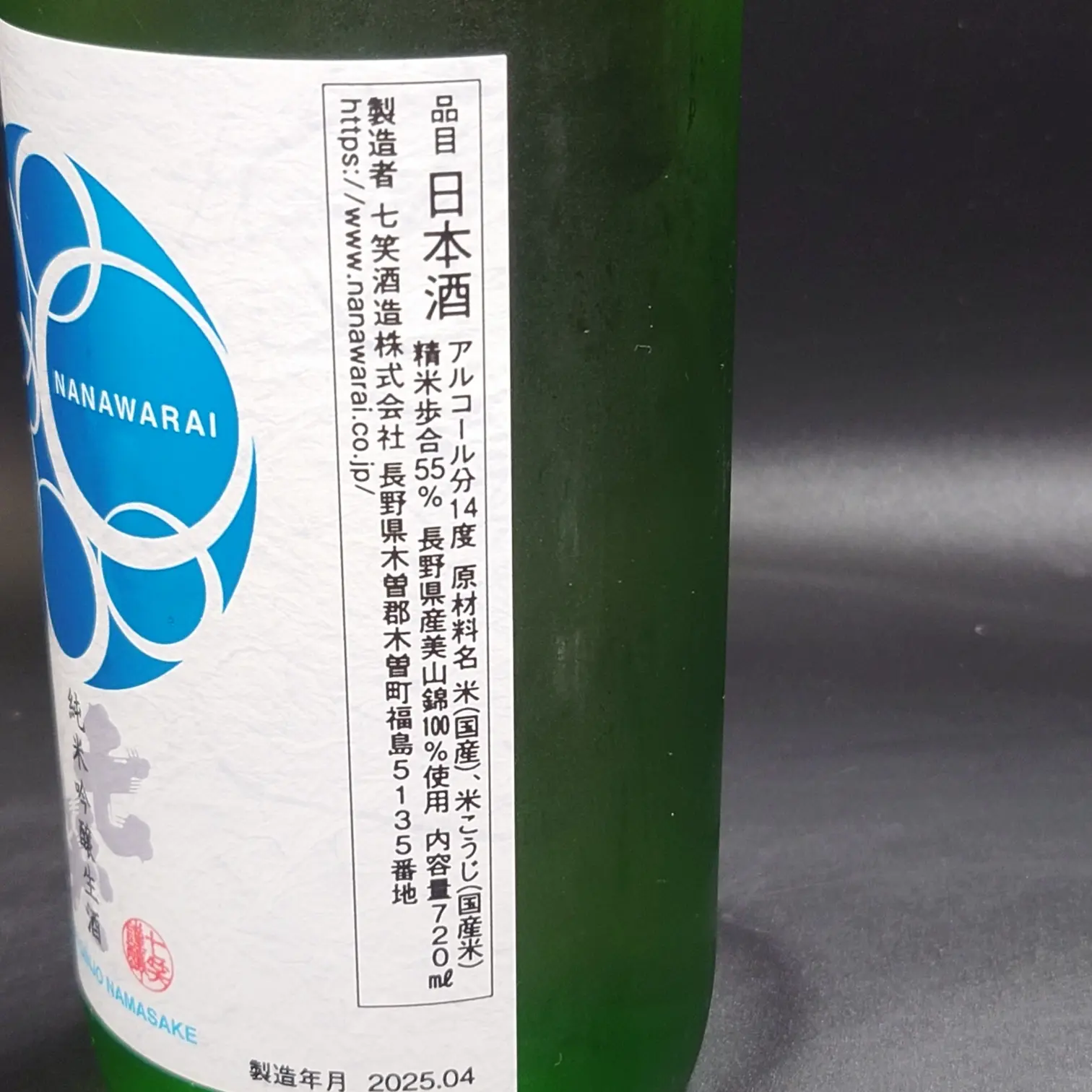 七笑 純米吟醸生酒の成分表示ラベル側面 アルコール14% 精米歩合55% 長野県産美山錦100%使用 内容量720ml 製造者七笑酒造の住所表記と公式URL 黒背景にグリーンボトル