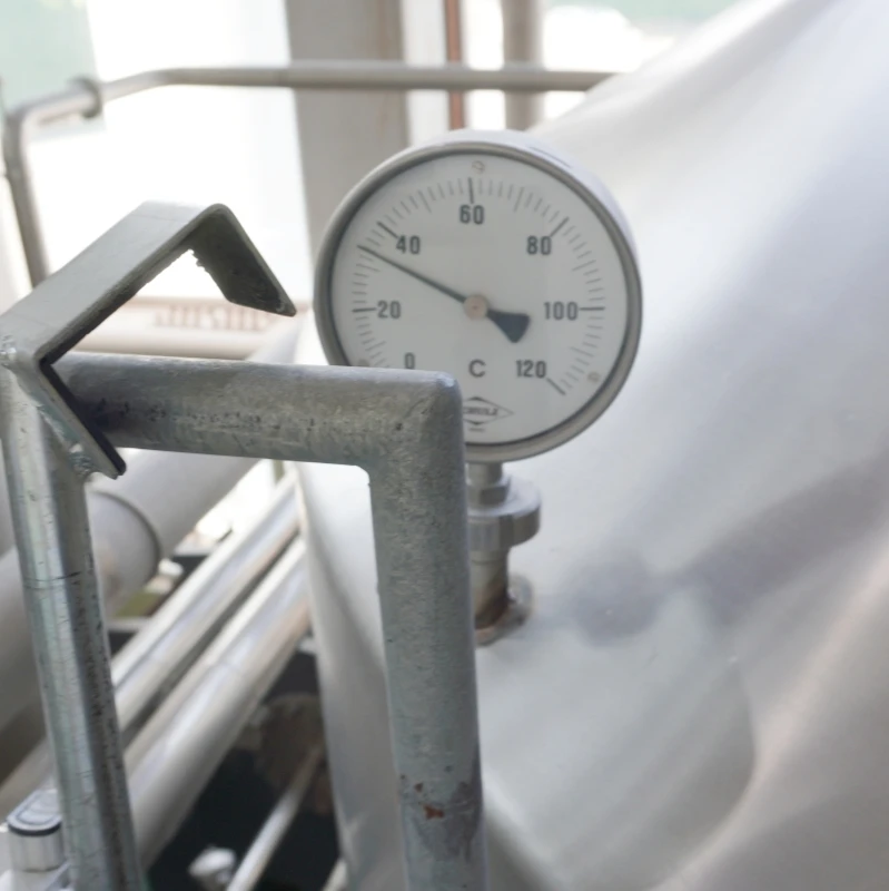第2章 仕込み釜の温度計|針は約60℃を指す 長野・佐久 ヤッホーブルーイング よなよなエールの醸造所見学 第2章|仕込み釜の温度計をクローズアップ 針は約60℃を指し 背後に配管と手すりが見える明るいブリューハウス