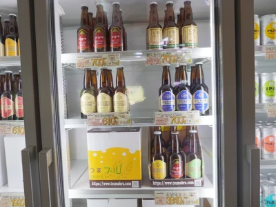 冷蔵ケースに並ぶ瓶ビールとつまブル箱 群馬・嬬恋高原ブルワリーの冷蔵ケース、赤や青のラベルが付いた瓶ビールと「つまブル」ロゴ入り箱が並ぶ様子