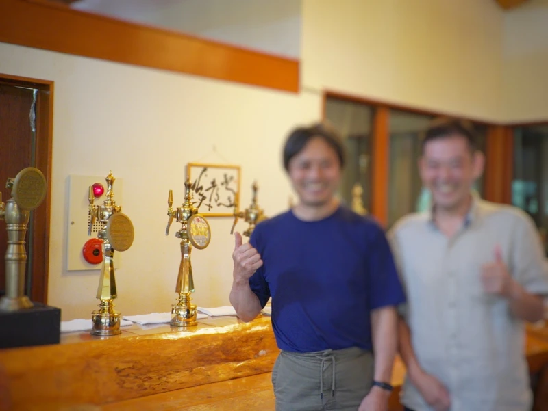 つまブル店内カウンター前の記念スナップ 嬬恋高原ブルワリーの店内カウンター前で、金色のビールタップを背景に並ぶスナップ