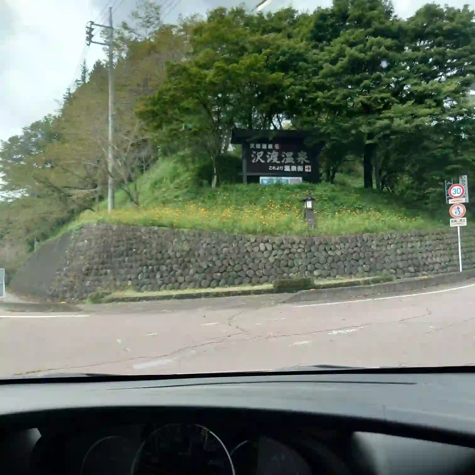 群馬県中之条町の沢渡温泉街入口。石垣の上に立つ木製の「沢渡温泉」看板が湯の里の始まりを告げる。