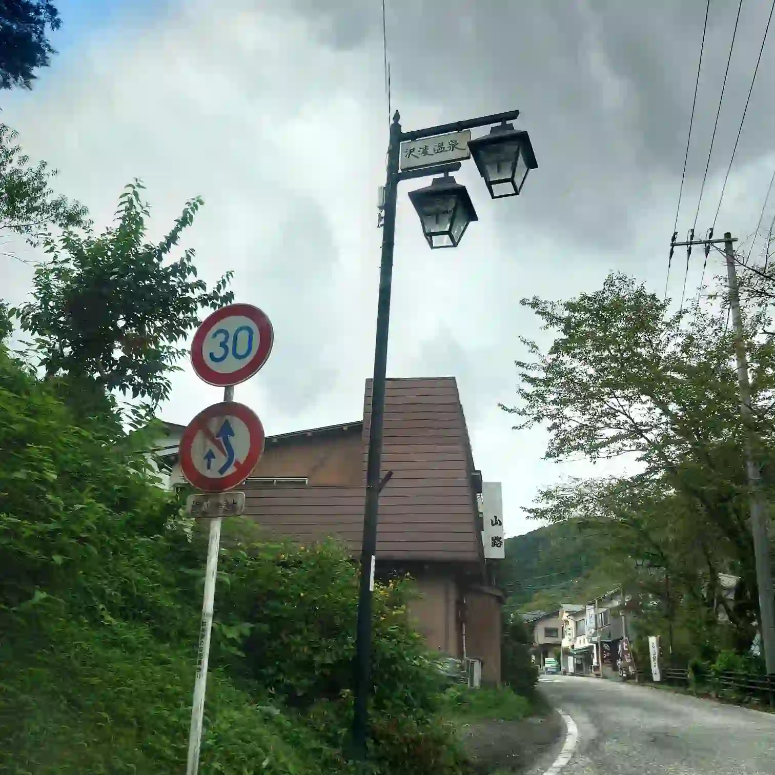 沢渡温泉入口付近の街灯に掲げられた案内板と、温泉街へ続く坂道の風景。