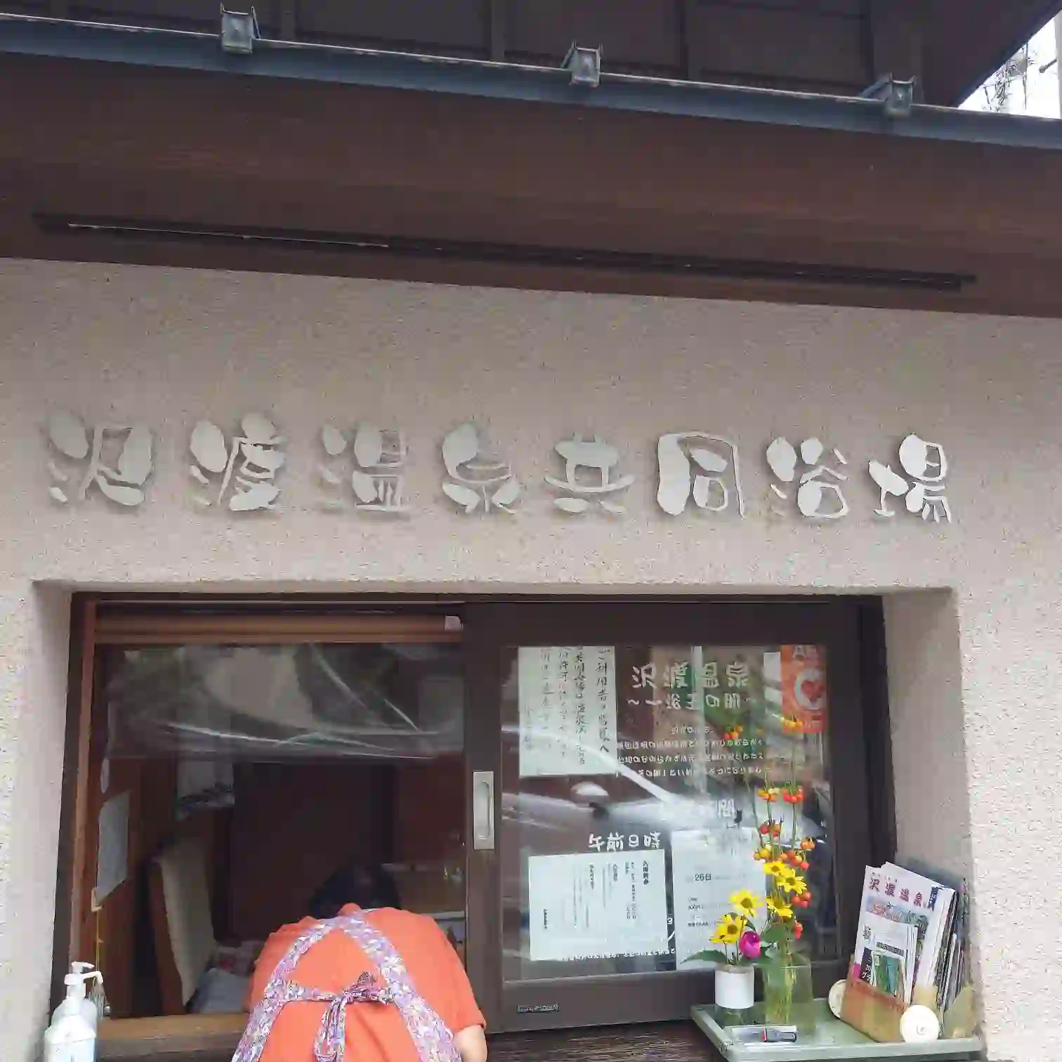 群馬県中之条町の沢渡温泉共同浴場 受付外観。優しい笑顔で迎える地元のおばちゃんと、壁に掲げられた立体文字の看板が印象的。