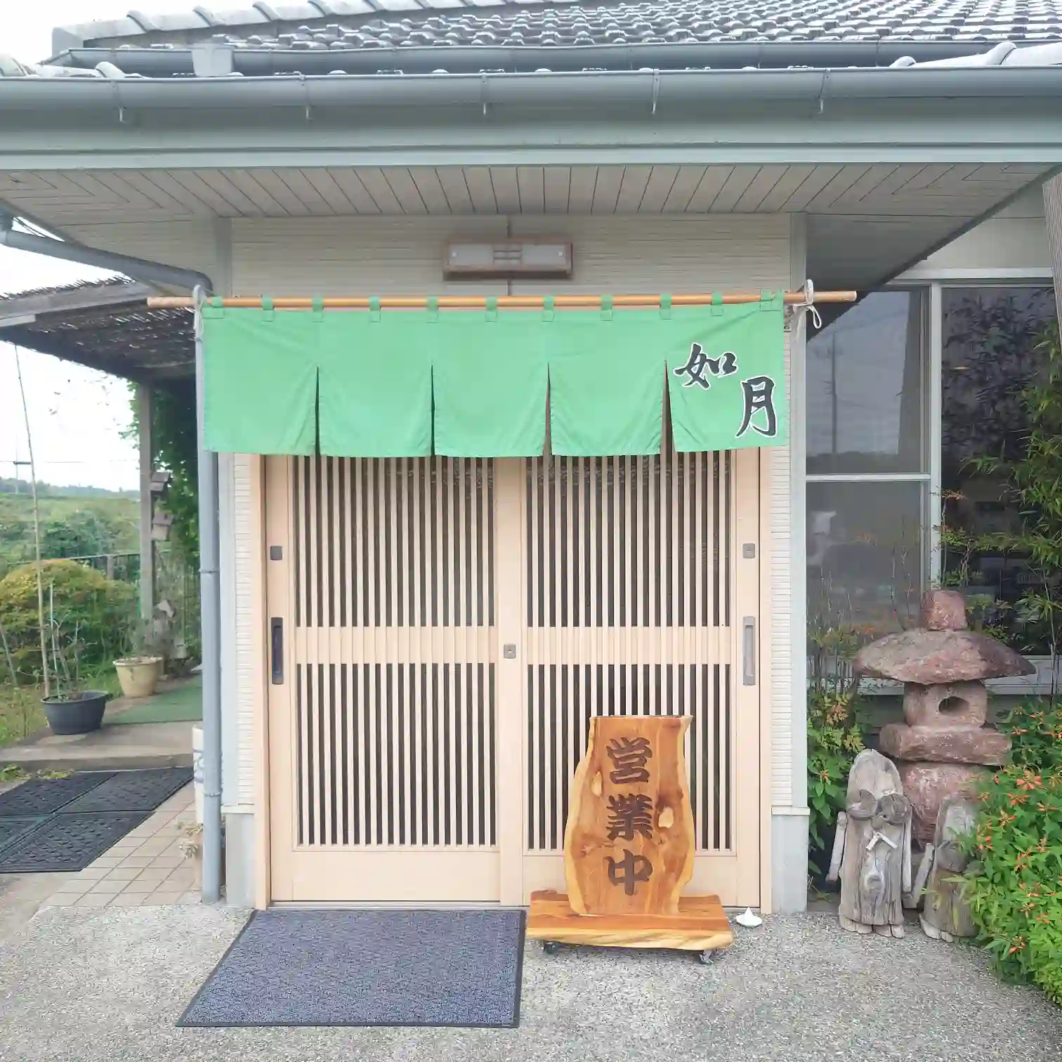 如月の入口外観 緑ののれんに「如月」の店名、木製の「営業中」看板が立つ入口外観
