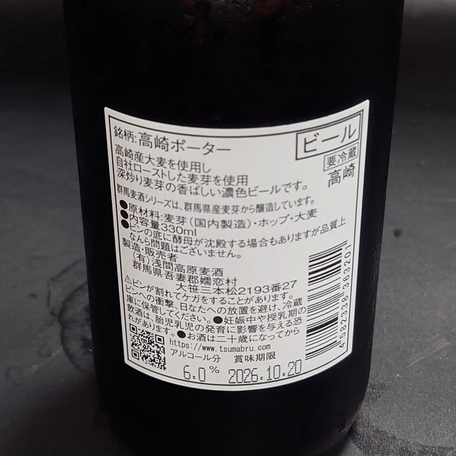 つまブル 高崎ポーター|裏ラベル(成分表示・330ml・アルコール6.0%) つまブル 高崎ポーターの裏ラベル 原材料表示 内容量330ml アルコール分6.0% 賞味期限2026-10-20 バーコードとQRコード 黒背景の自宅撮影