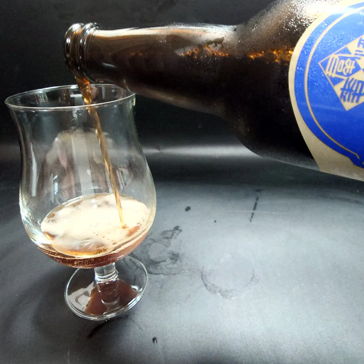 つまブル 高崎ポーター|注ぎ途中の流れと立ち上がる泡(チューリップグラス) つまブル 高崎ポーターをチューリップグラスへ注ぐ途中 濃いこげ茶〜琥珀の液色にベージュの泡が立ち上がる 青ラベルのボトル 黒背景 自宅撮影