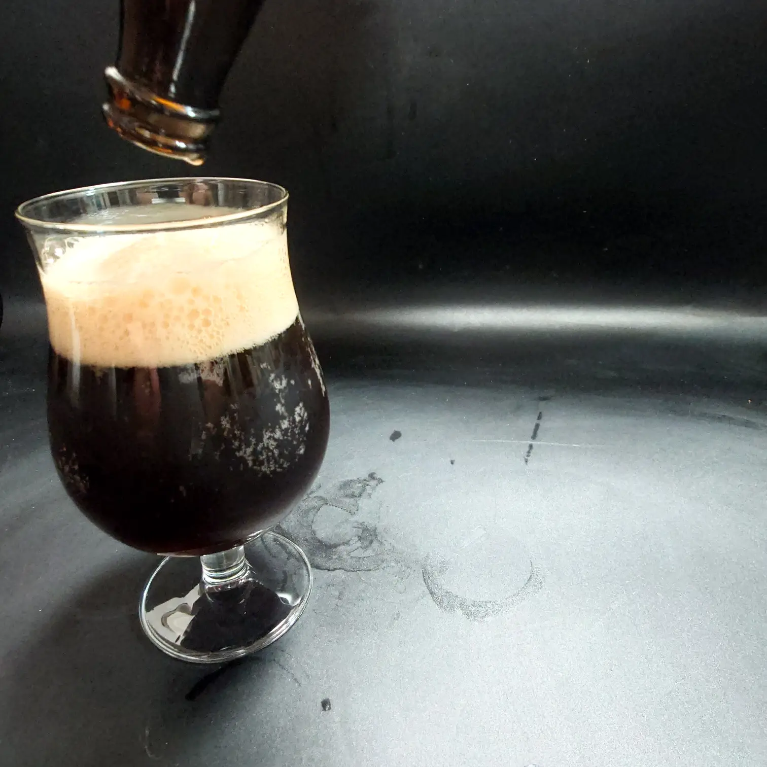 つまブル 高崎ポーター|注ぎ終えのグラスと立ち上がるベージュ泡 つまブル 高崎ポーターを注ぎ終えたチューリップグラス こげ茶〜黒の液色にベージュの泡が盛り上がる 上部にボトル口が見える 黒背景 自宅撮影