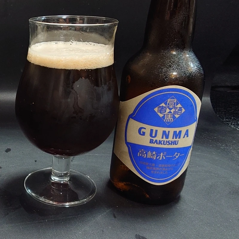 つまブル 高崎ポーター|グラスとボトルのツーショット(青ラベル) つまブル 高崎ポーターのチューリップグラスと青ラベルのボトルを並べて ベージュ泡が乗る濃いこげ茶の液色 黒背景で結露 自宅撮影