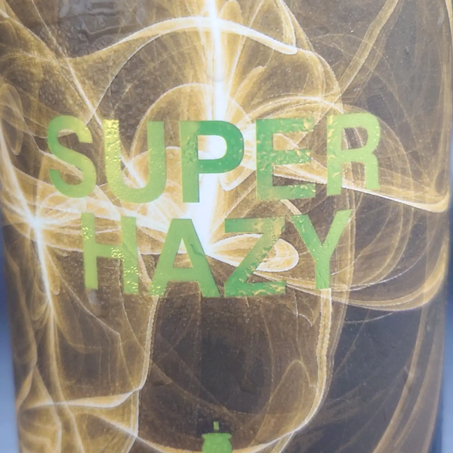 宇宙ブルーイング SUPER HAZY|メッキ風ゴールドロゴとスモーク調ゴールドが印象的なラベル接写 宇宙ブルーイング「SUPER HAZY」ラベルの接写、渦巻く金色のスモーク調デザインにメッキ風ゴールドのロゴが浮かぶ