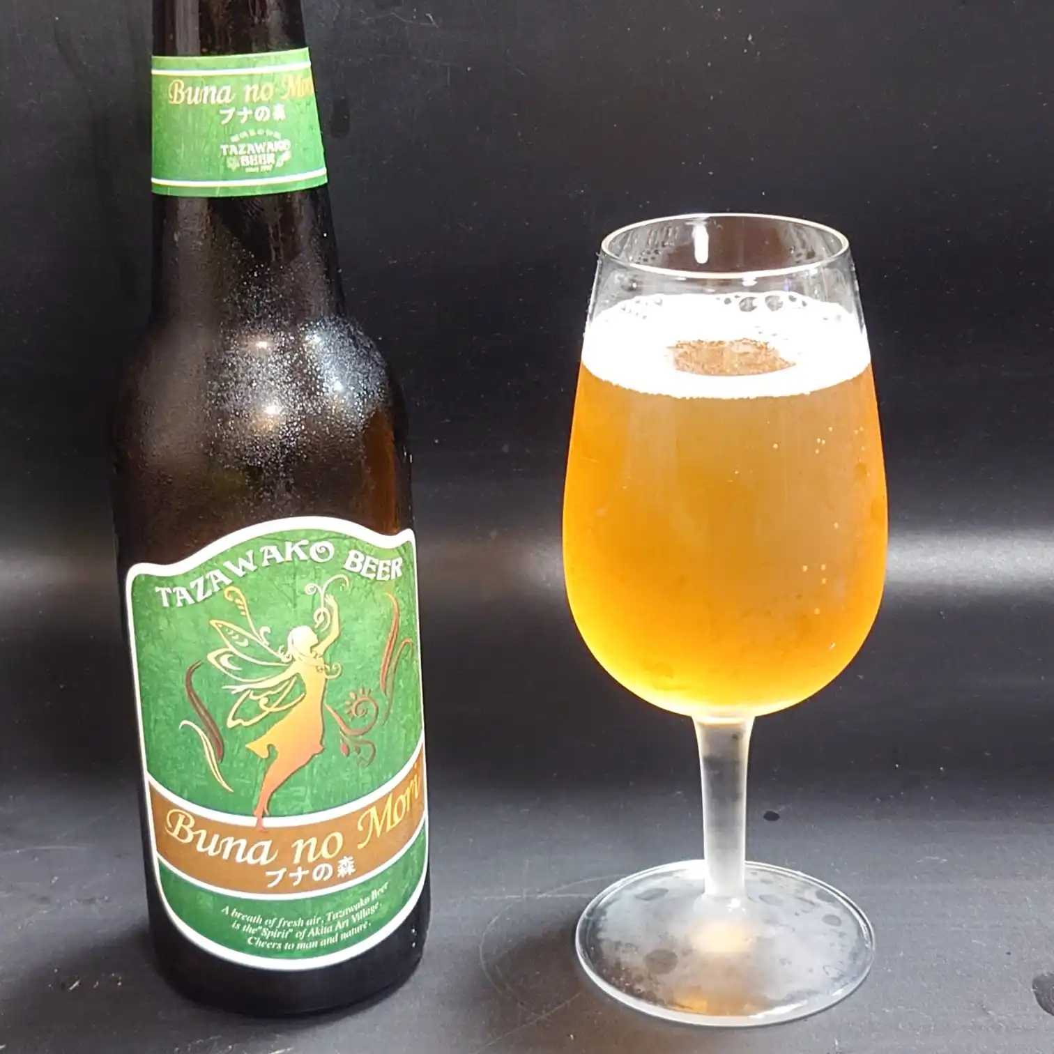 田沢湖ビール『ブナの森』のボトルとグラスを並べたショット。黄金色の液体が光を受けて輝き、妖精ラベルのデザインが際立つ