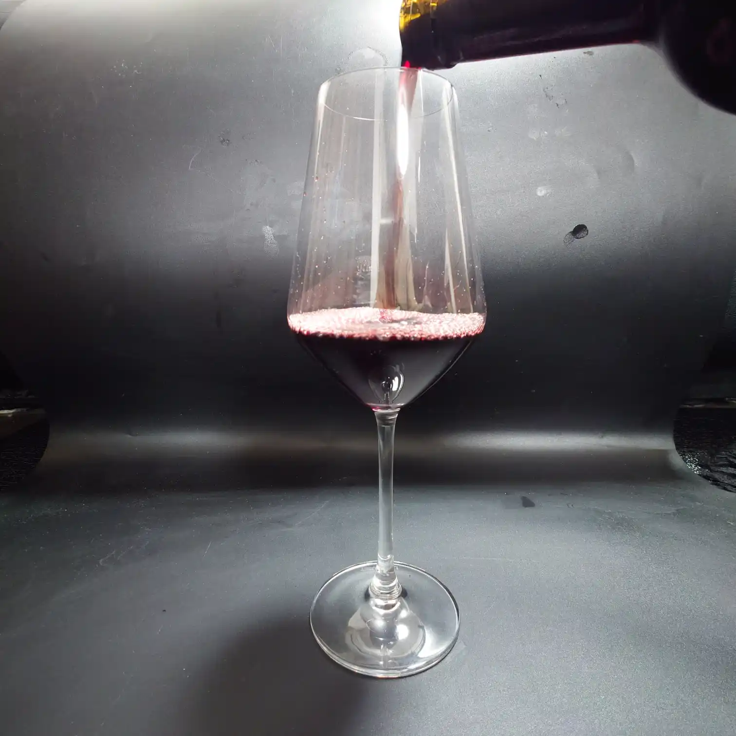 カークランド ボルドー・シュペリュール 2022 グラスに満ちる深紅 カークランド ボルドー・シュペリュール2022をグラスに注ぎ続けるシーン。泡立つ縁と濃厚な赤紫の液面が力強い印象を与える。