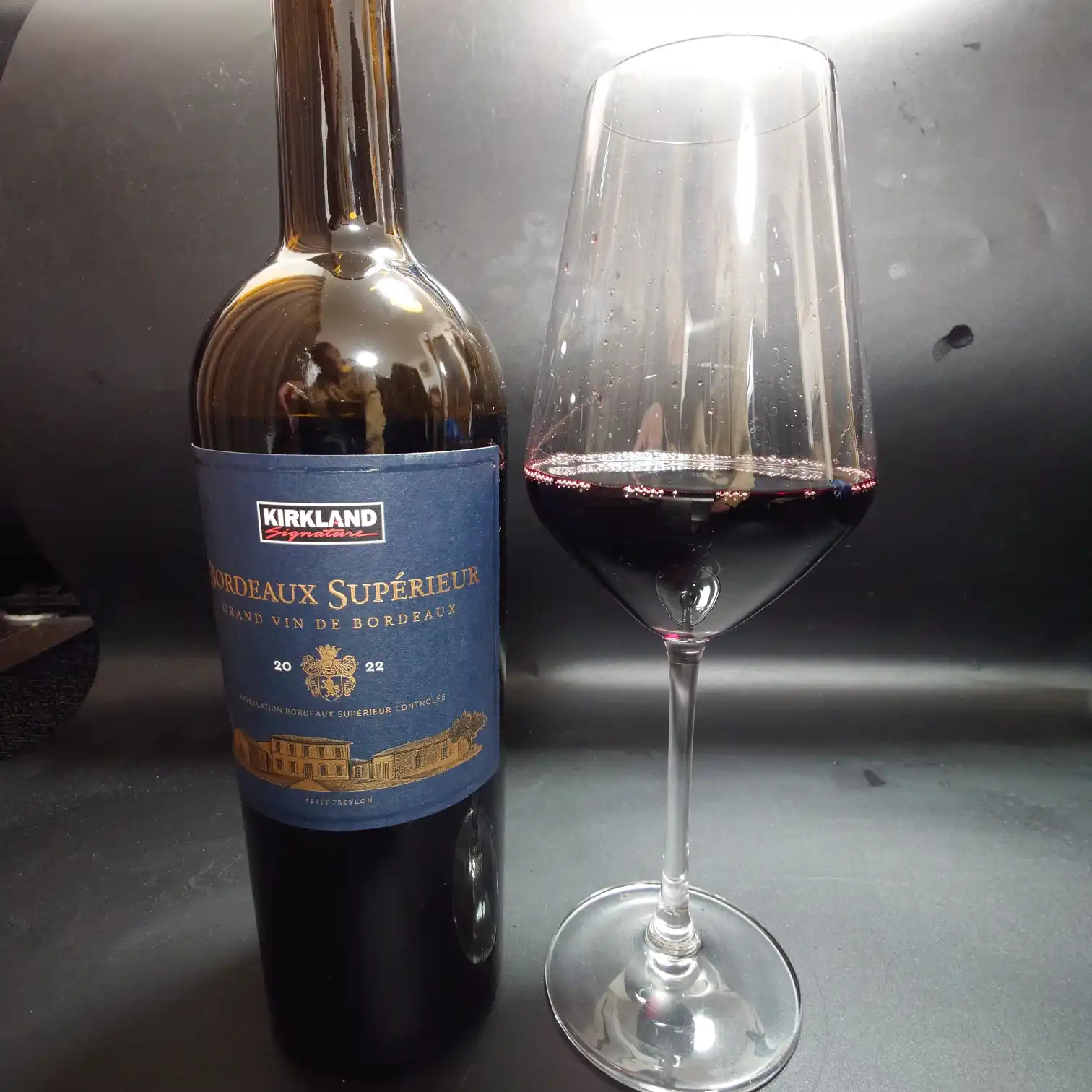 カークランド ボルドー・シュペリュール 2022 ボトルとグラス カークランド ボルドー・シュペリュール2022のボトルと注いだグラスを並べた写真。深いルビー色のワインがグラスに映え、ラベルの紺と好対照をなす。