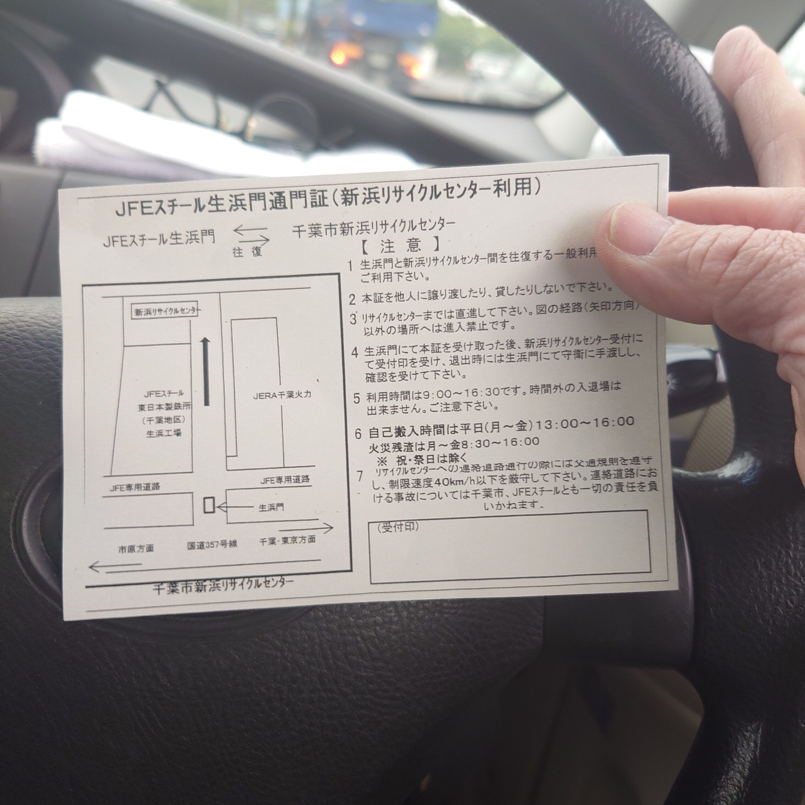 新浜リサイクルセンターへ向かう車内で、JFEスチール生浜門通用口案内の紙を手に持ち、搬入ルートと注意事項を確認している様子。