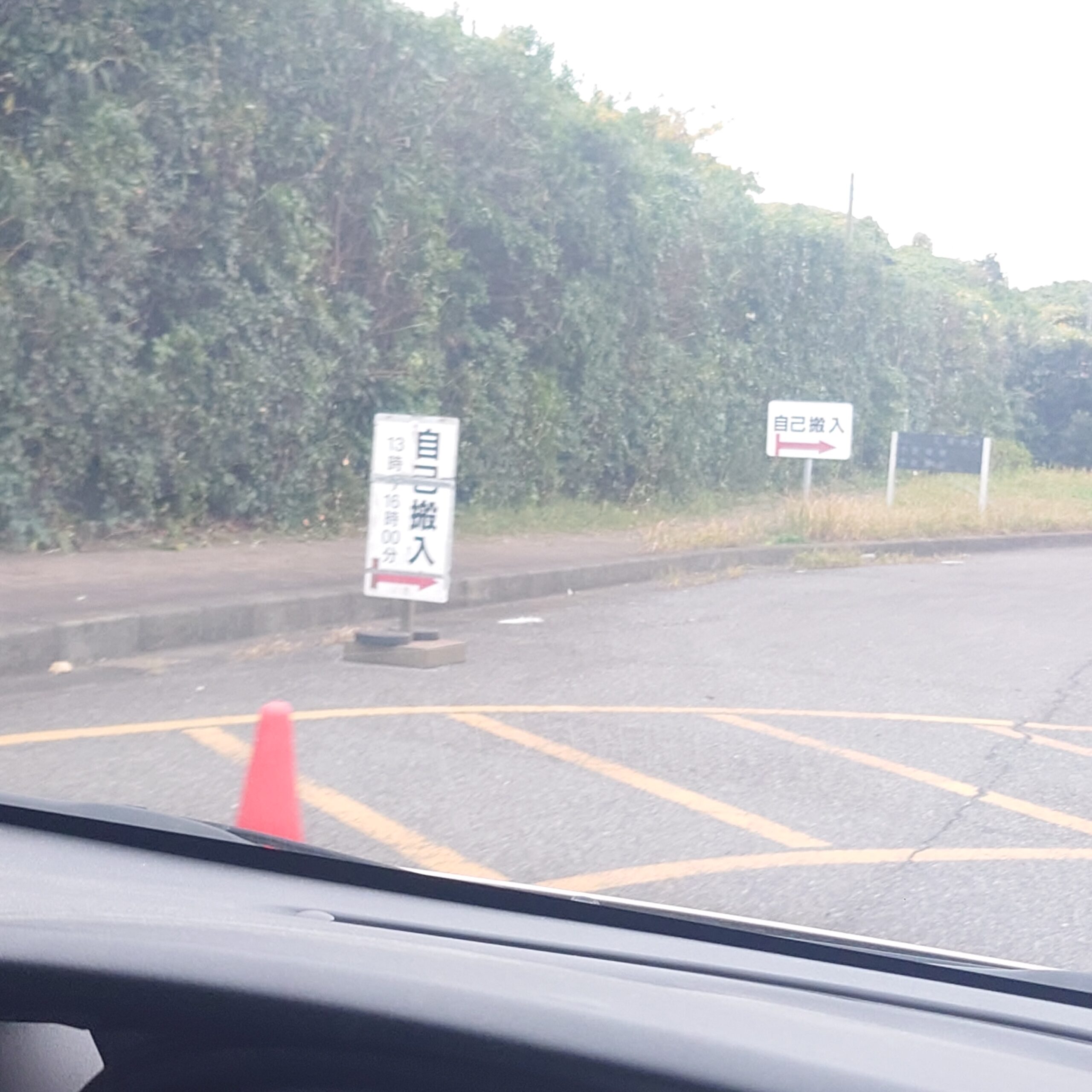 新浜リサイクルセンターの入口付近で、車内から見える『自己搬入』の案内看板と誘導コーン。センターへの搬入口を示している様子。
