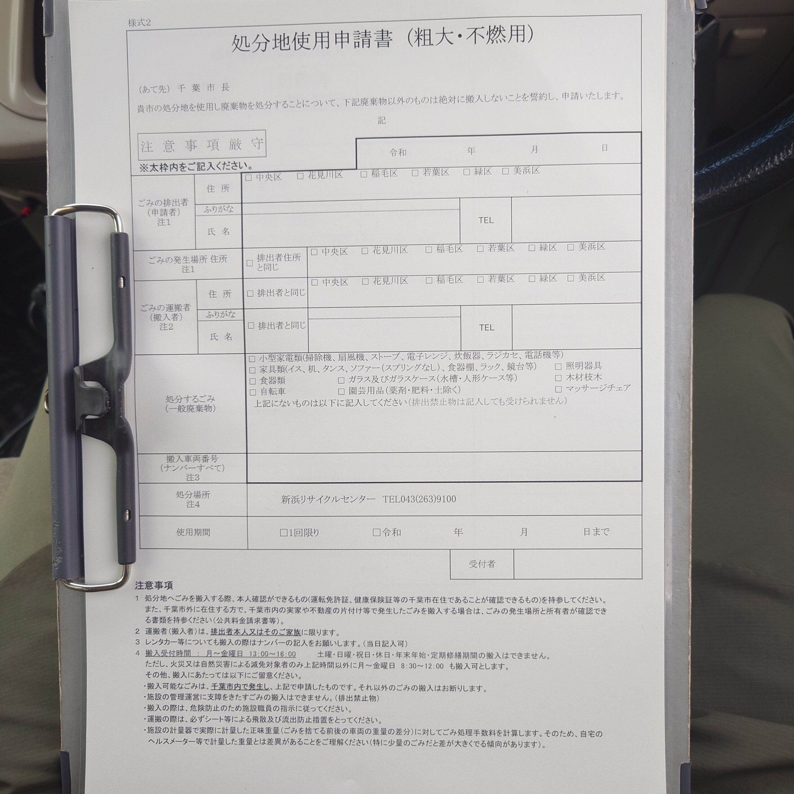 新浜リサイクルセンターで粗大・不燃物の搬入時に使用する『処分地使用申請書』を、車内でクリップボードに挟んだまま記入している様子。