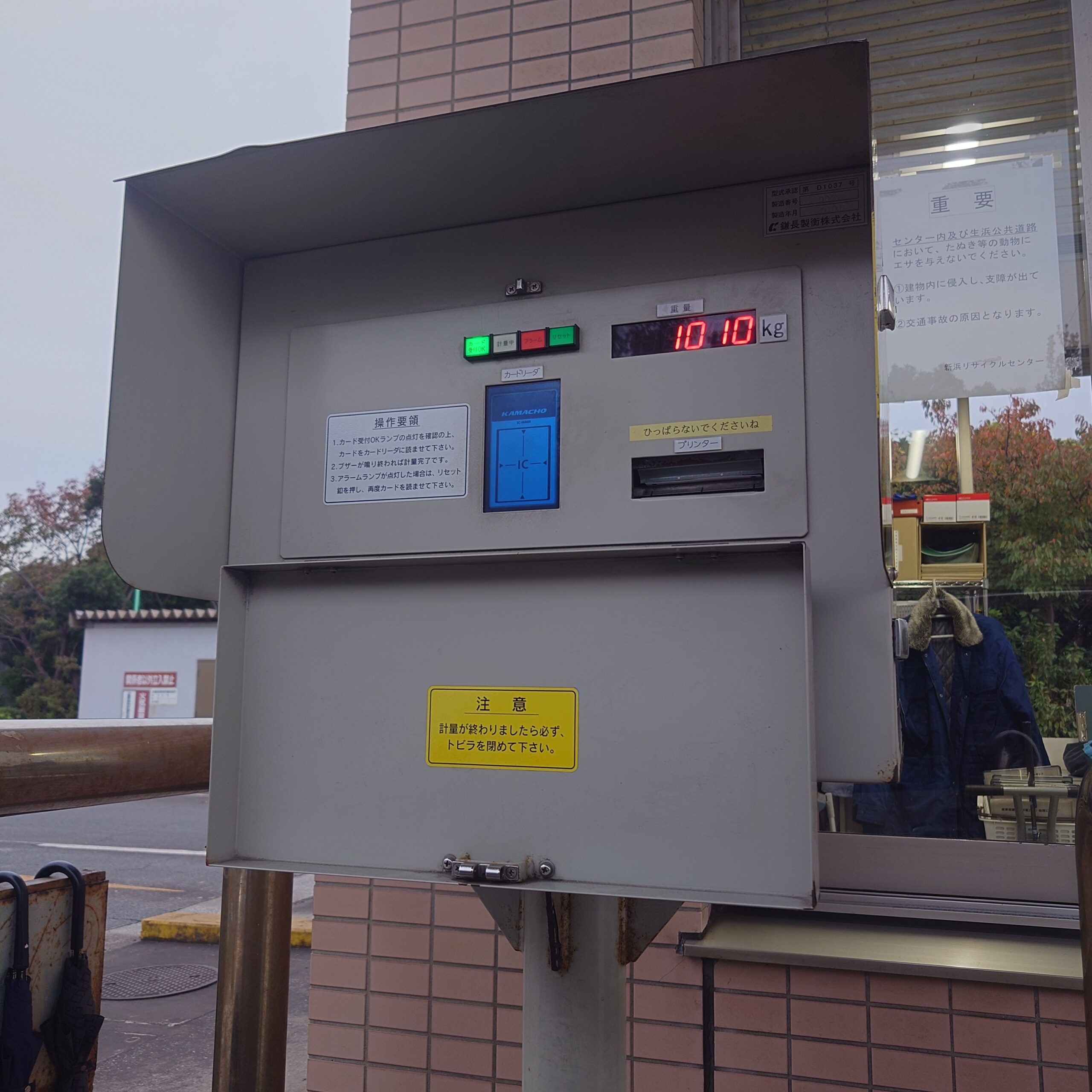 新浜リサイクルセンターの計量機で、搬入車両の重量を計測している様子。電子表示には重量が表示され、計量レーン横の装置が写っている。