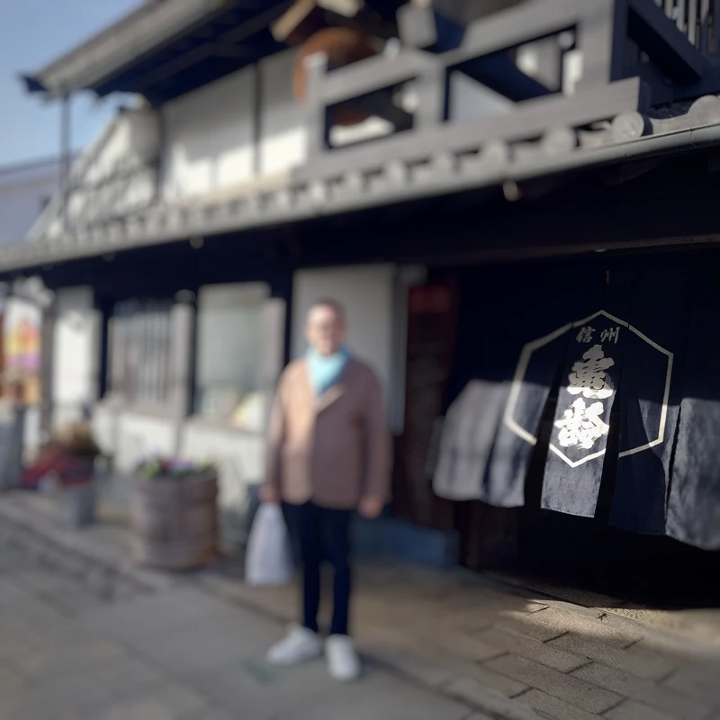 長野県上田市　信州亀齢の暖簾が掛かる酒蔵の店先、買い物袋を手にしたチェックイン前の寄り道ショット