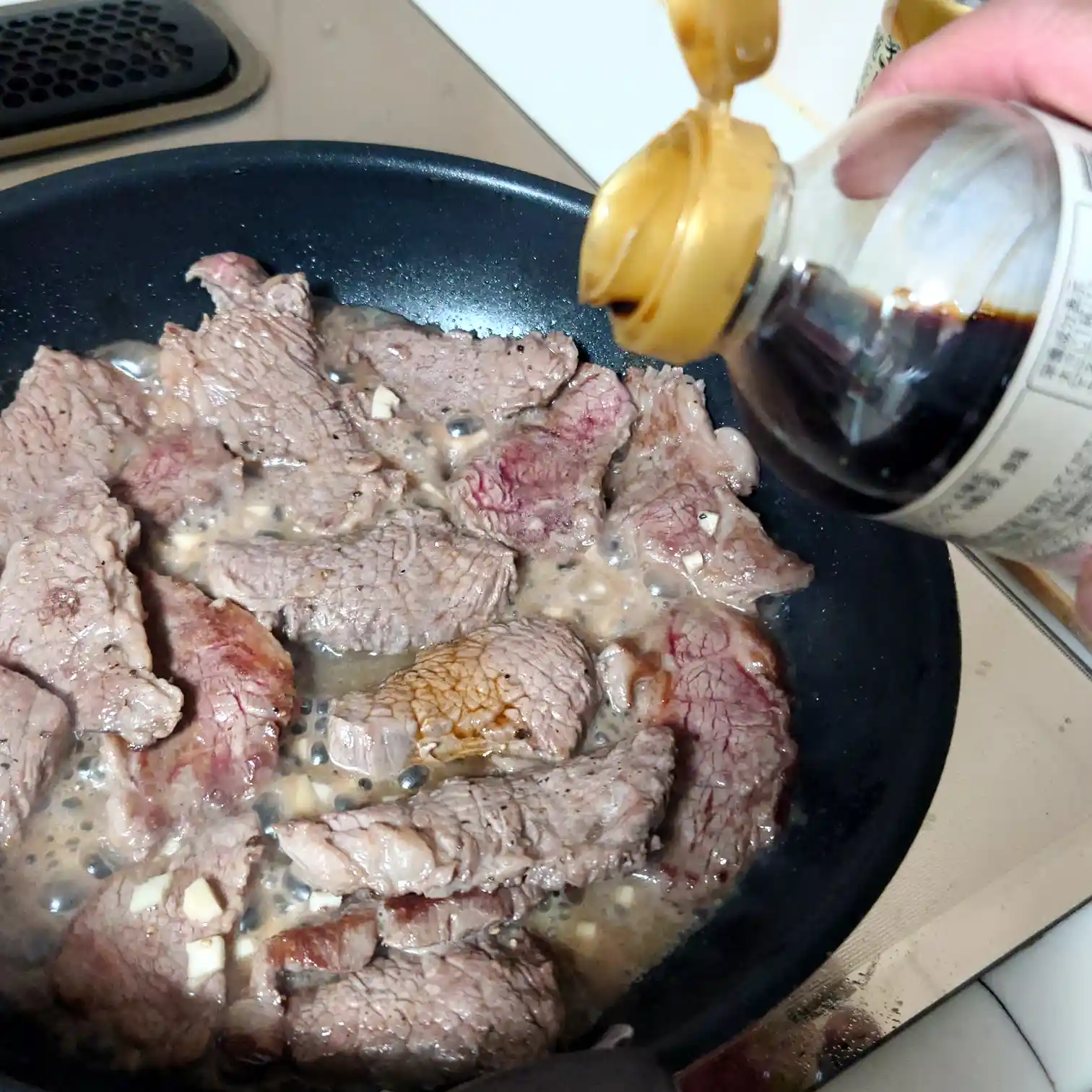 ガーリックバターで焼いたリブキャップにしょうゆを回し入れて香ばしさを足す工程　仕上げの香り付けの瞬間