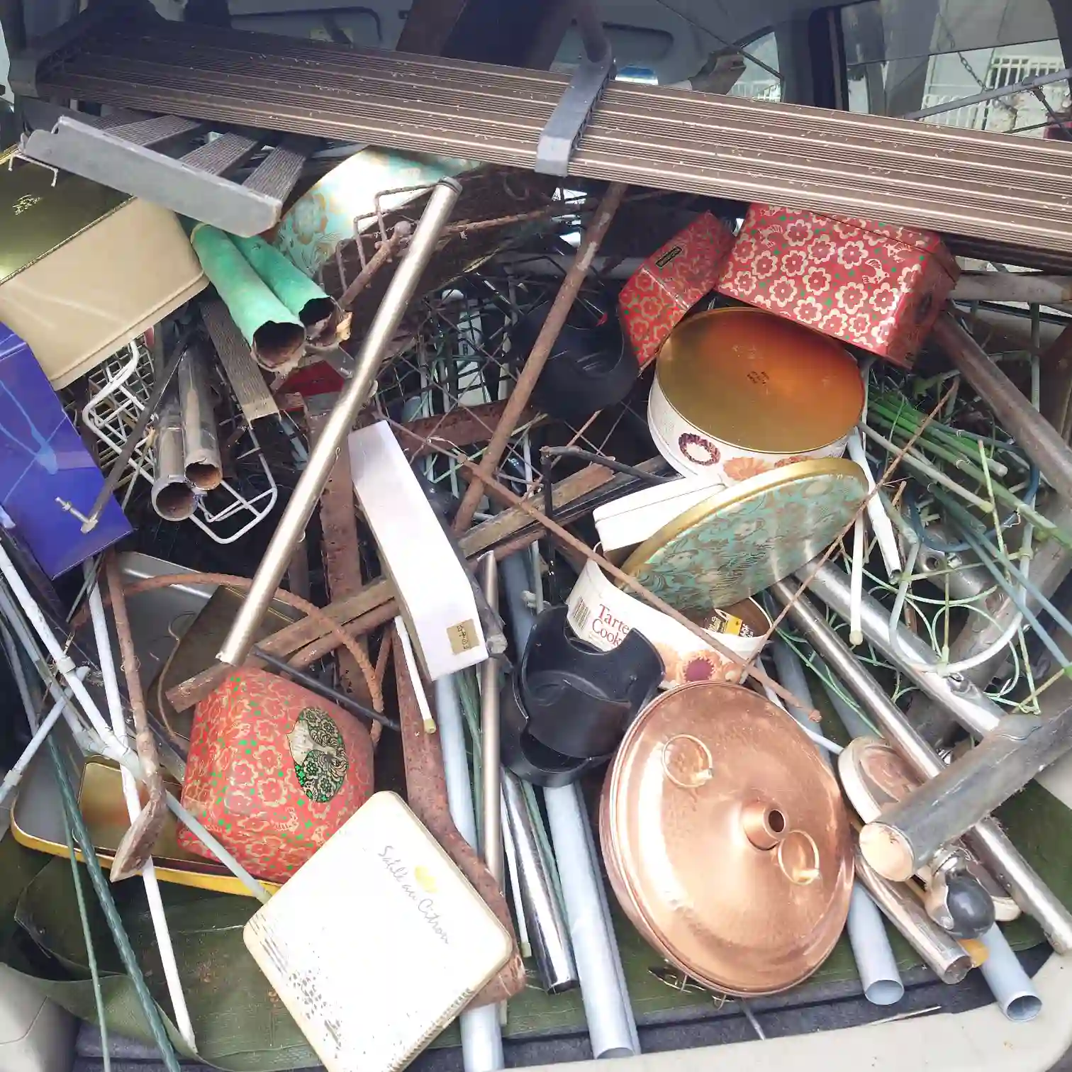 軽自動車の荷台に再び満載された鉄くず。今回は古いクッキーの空き缶や細かい金属ゴミが多く、隙間なく詰め込まれている。母が小物の収納に使っていた生活の跡が垣間見える。
