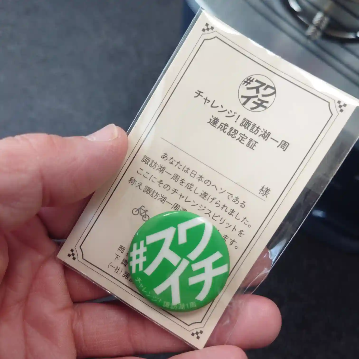 スワイチ（諏訪湖一周）達成認定証と、緑色をした公式記念缶バッジ