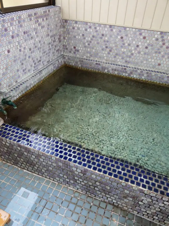 青いタイル張りの趣ある小さな温泉浴槽。透明な湯が静かに満ちている