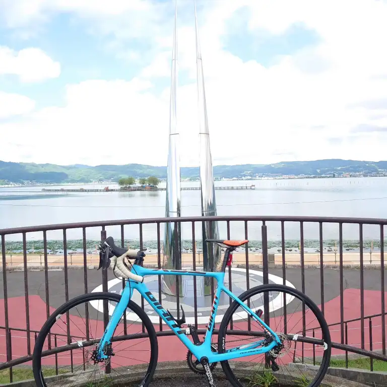 諏訪湖のサイクリングロードに停車したロードバイク。背景に広がる湖面と遠くの山々