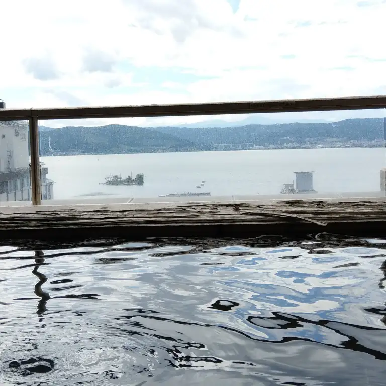 上諏訪温泉の露天風呂から望む諏訪湖。湯面が鏡のように空を映し出している風景